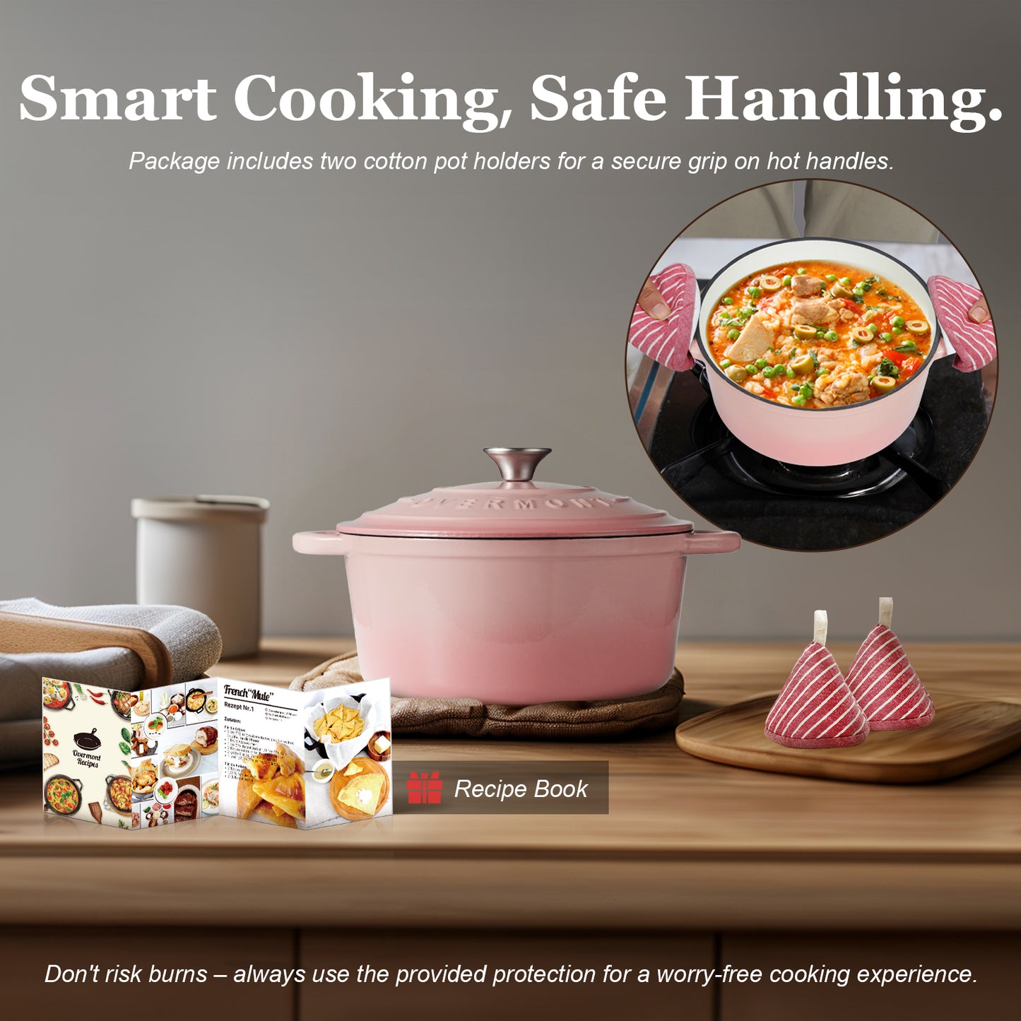 Pink cast iron pot with accessories on a wooden surface, including a recipe book and pot holders.